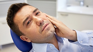 Man in dental chair holding jaw